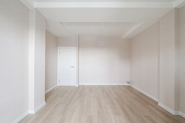 bright, empty room with light-colored wooden floors, neutral walls, a white door, and a layered ceiling. The space is clean and appears to be newly renovated