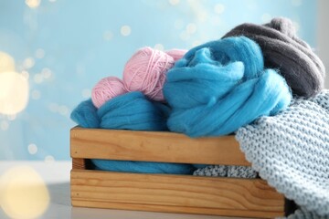 Soft felting wool and knitting yarn in crate on white wooden table against light blue background...