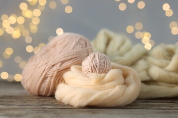 Soft felting wool and yarns on wooden table against grey background with blurred lights, closeup