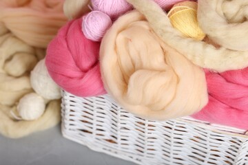 Soft felting wool and yarns in wicker basket on grey table, closeup