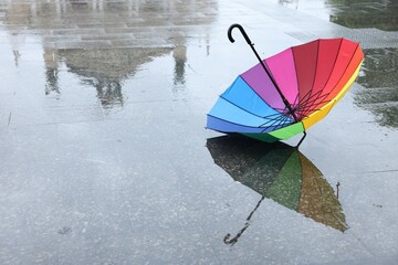 Colorful umbrella on wet asphalt outdoors, space for text