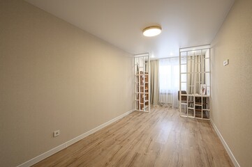 Bright room with beige walls, wooden floor, and white decorative dividers. Natural light filters...