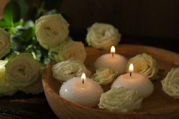 Burning candles, water and rose flowers in bowl on wooden table, closeup