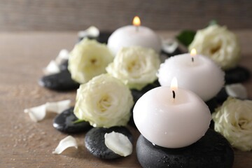 Burning candles, stones and rose flowers on wooden table, closeup