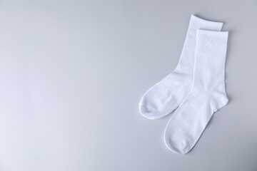 Pair of comfortable white socks on light gray background, top view. Space for text