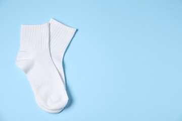 Pair of comfortable white socks on light blue background, top view. Space for text