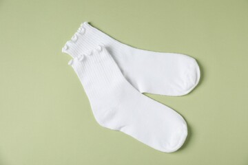 Pair of comfortable white socks on light green background, top view