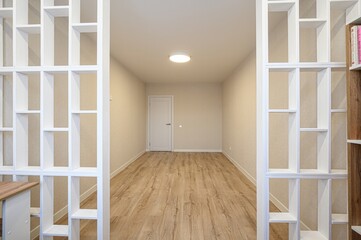 shot of an empty room through decorative shelving. Room features light wood floors, light beige...