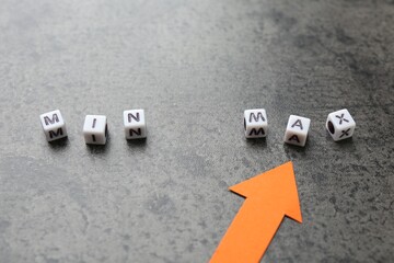 Words Min and Max made of cubes with arrow pointing at it on grey table, closeup