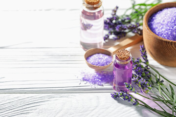 Bottles of lavender essential oil, sea salt and flowers on white wooden table, closeup. Space for...