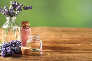 Bottles of lavender essential oil and flowers on wooden table, closeup. Space for text