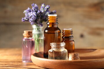 Bottles of lavender essential oil and flowers on wooden table, closeup