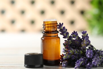Bottle of essential oil and flowers on white wooden table, closeup