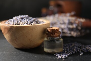 Bottle of essential oil and lavender flowers on black table, closeup