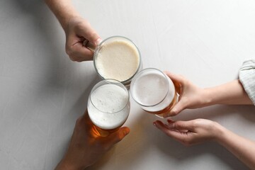 Friends clinking glasses of beer at white table, top view