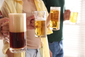 Friends with glass mugs of beer indoors, closeup