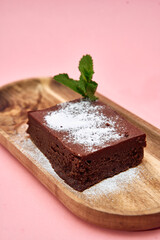 Decadent chocolate brownie with mint leaf garnish on rustic wooden plate