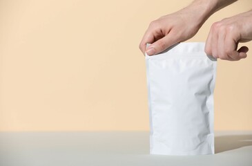 Woman holding blank zipper stand-up pouch at grey table against beige background, closeup. Space...