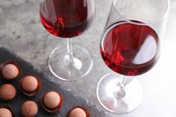 Red wine in glasses and truffle bonbons on grey textured table, selective focus