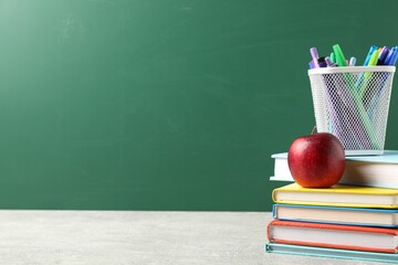 Different school stationery and red apple on grey table against blackboard, space for text