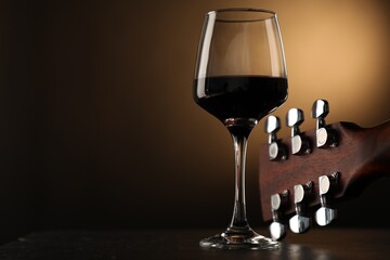 Acoustic guitar and glass of red wine on black table, closeup. Space for text