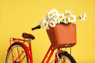 Bicycle with basket of beautiful flowers on yellow background, closeup
