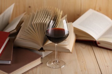 Glass of red wine and books on wooden table, closeup