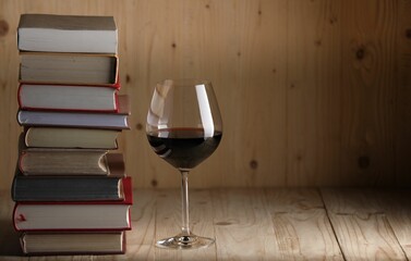 Glass of red wine and stacked books on wooden table. Space for text