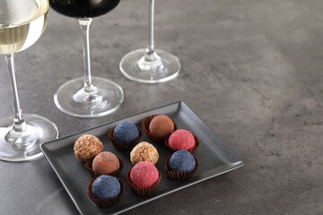 Tasty truffle bonbons and wine on grey table, above view. Space for text
