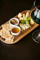 Gourmet cheese board with crackers grapes and red wine on wooden serving platter