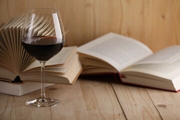 Glass of red wine and open books on wooden table, closeup. Space for text