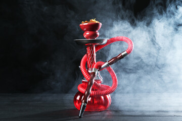 Hookah on wooden table with smoke against black background