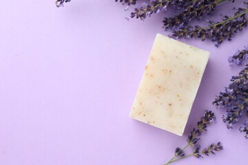 Aromatic soap bar and lavender flowers on violet background, flat lay. Space for text