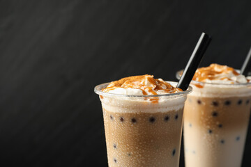 Tasty milk bubble tea in plastic cups on black background, closeup. Space for text