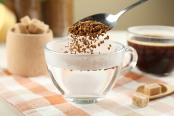 Putting instant coffee into cup at light table, closeup