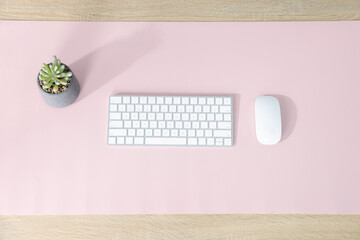 Computer keyboard, mouse, houseplant and pink mousepad on wooden table at workplace, flat lay
