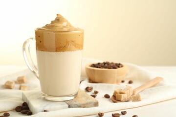 Delicious dalgona coffee in glass cup, beans and brown sugar on light table, closeup