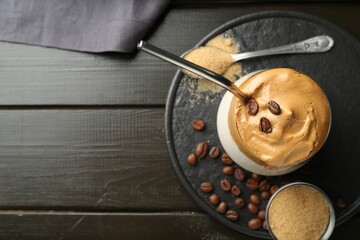 Delicious dalgona coffee in glass, beans and brown sugar on wooden table, top view. Space for text