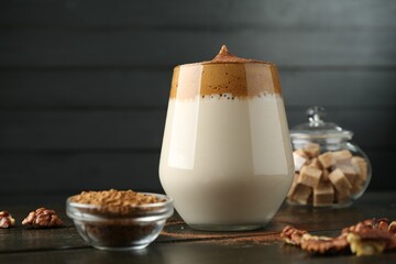 Delicious dalgona coffee in glass, granules, walnuts and brown sugar on wooden table, closeup