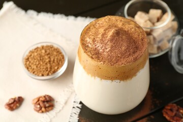Delicious dalgona coffee in glass, granules, walnuts and brown sugar on wooden table, above view