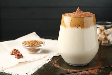 Delicious dalgona coffee in glass, granules, walnuts and brown sugar on wooden table, closeup