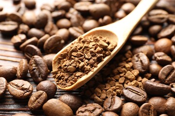 Spoon with instant coffee and beans on wooden table, closeup