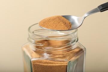 Taking instant coffee with spoon on beige background, closeup