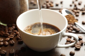 Pouring hot water into cup with instant coffee at wooden table, closeup