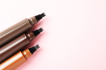 Liquid eyebrow pencils on light pink background, flat lay. Space for text