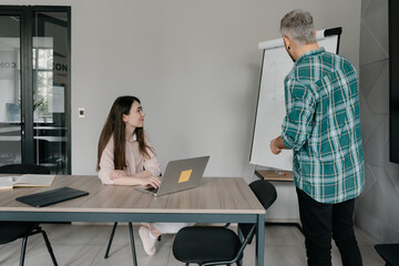 Two coworkers discussing a presentation, utilizing a flip chart in a modern office