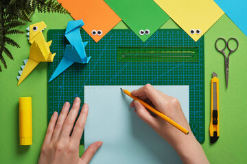 Making an origami dinosaur. The hand draws a pattern for cutting out on paper. Around are items for...
