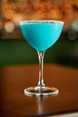 Elegant blue cocktail with salt rim and bokeh lights in background on wooden table