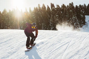 Snowboarder performing jump trick on sunlit snowy slope with pine forest background, fresh powder...