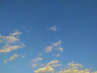The bright blue sky stretched out with scattered white clouds, illuminated by the sunlight that...